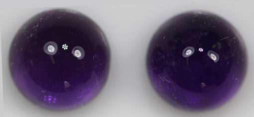 Two purple amethyst cabochons on a white surface.