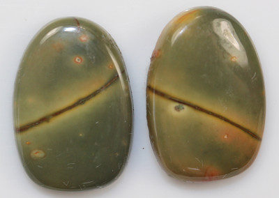 A pair of oval green jasper cabochons on a white surface.