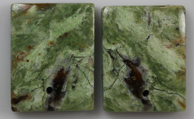 A pair of green jade cabochons on a white surface.