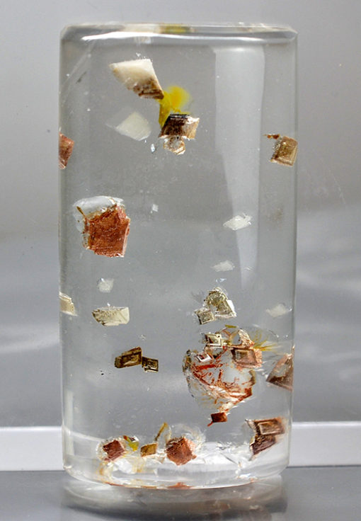 A glass of water with a few pieces of paper floating in it.
