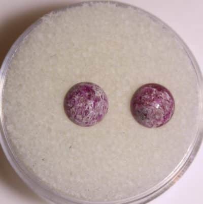 A pair of purple gemstone studs in a glass container.