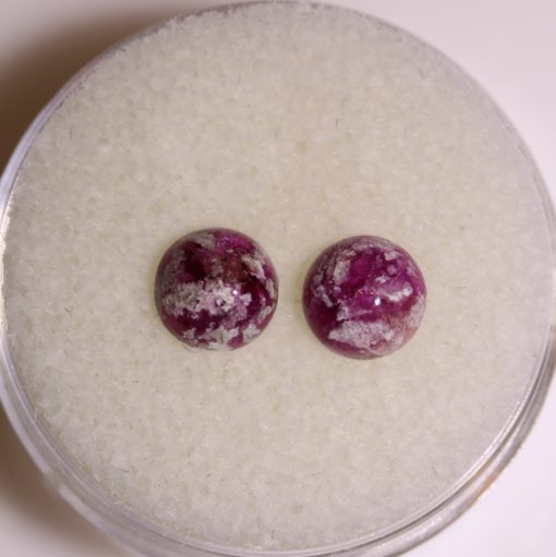 A pair of purple gemstone studs sitting on top of a white surface.