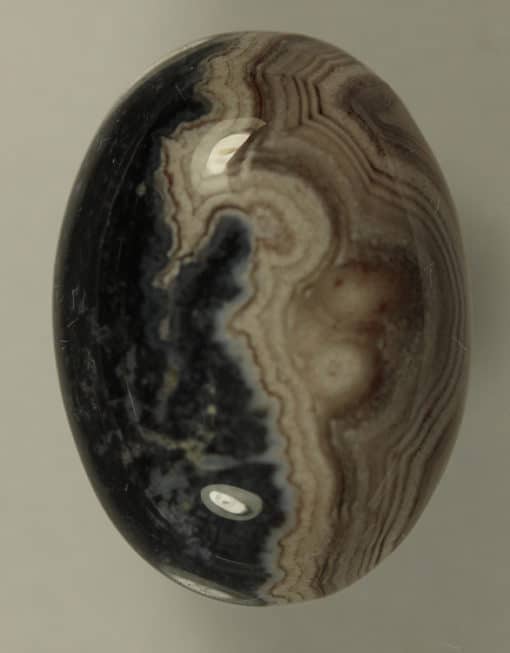 A Banded Agate 8.85cts Oval Cabochon 18.00 x 11.00mm Q0324 on a white surface.