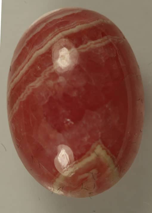 A Rhodocrosite 12.95cts Oval cabochon ball on a white surface.