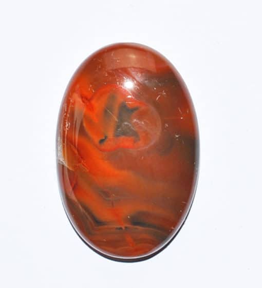 An orange and black agate oval cabochon on a white surface.