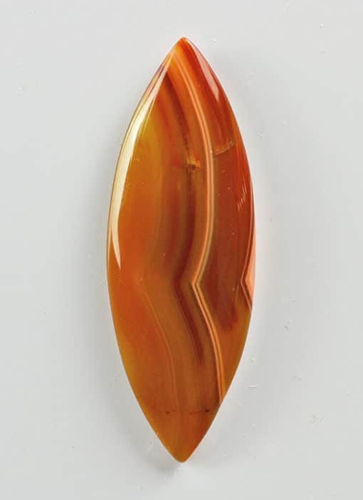 An orange agate leaf pendant on a white surface.