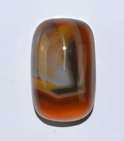 An orange and brown agate cabochon on a white surface.