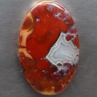 A red and white agate pendant on a metal surface.