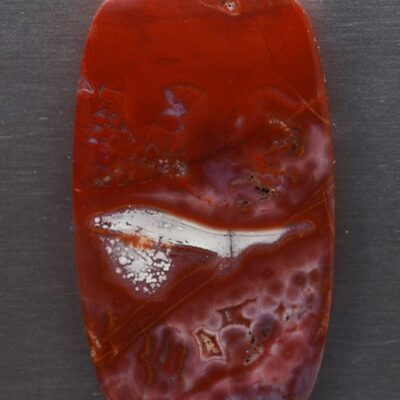 A red and white agate pendant on a metal surface.