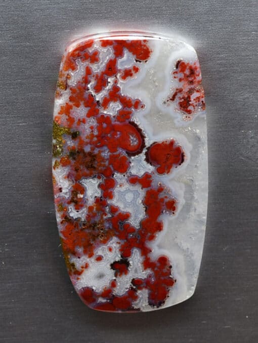 A red and white agate pendant on a metal surface.