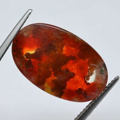 An orange opal stone is being held by a pair of pliers.