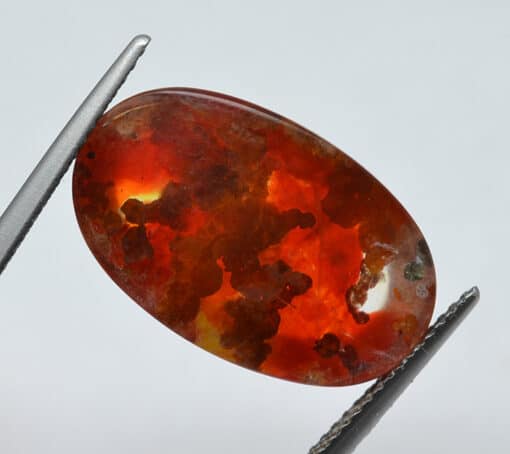 An orange opal stone is being held by a pair of pliers.