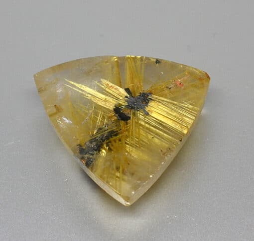 A triangular piece of yellow quartz on a white surface.