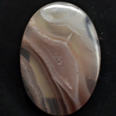 A brown and white agate cabochon on a black surface.