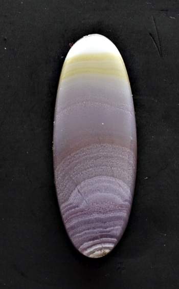 A purple and yellow oval agate stone on a black surface.