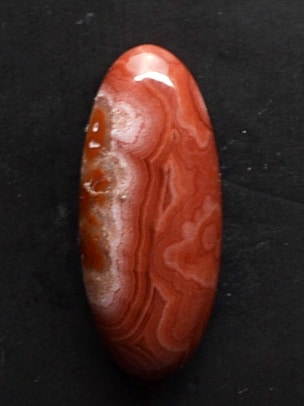 A red agate oval cabochon on a black surface.