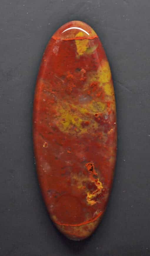 A red and yellow oval shaped stone on a black surface.