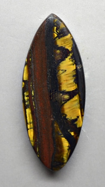 A black and yellow tiger eye cabochon on a white surface.