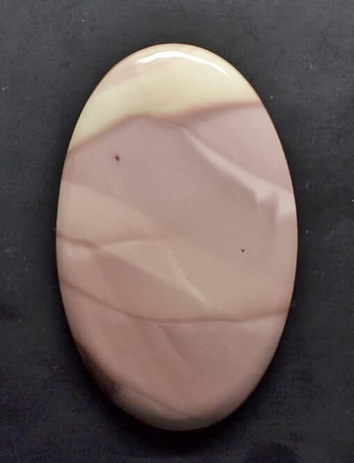 A pink and white oval shaped stone on a black surface.