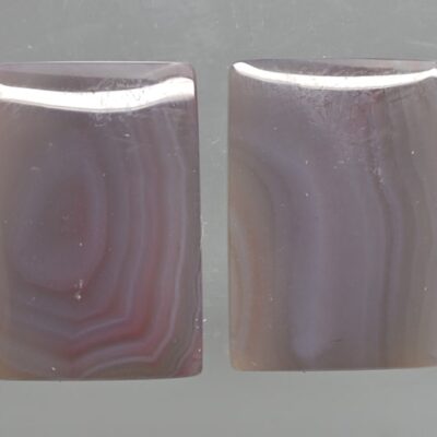 A pair of purple agate cabochons on a gray surface.