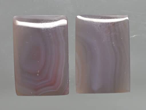 A pair of purple agate cabochons on a gray surface.