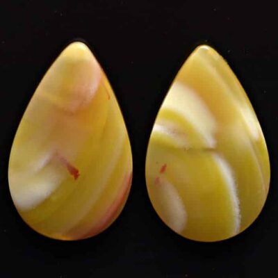 Two yellow jade tear shaped cabochons on a black surface.