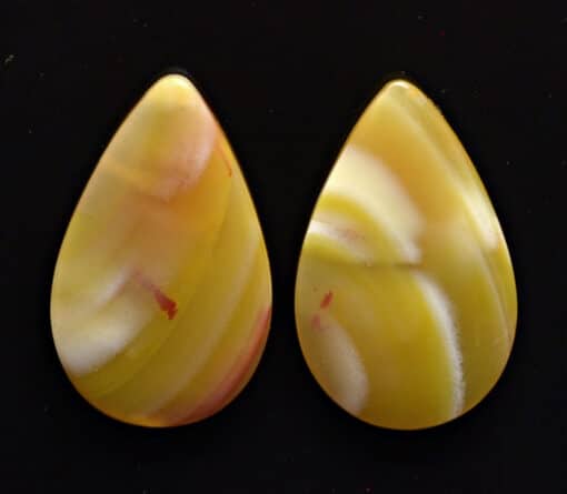 Two yellow jade tear shaped cabochons on a black surface.