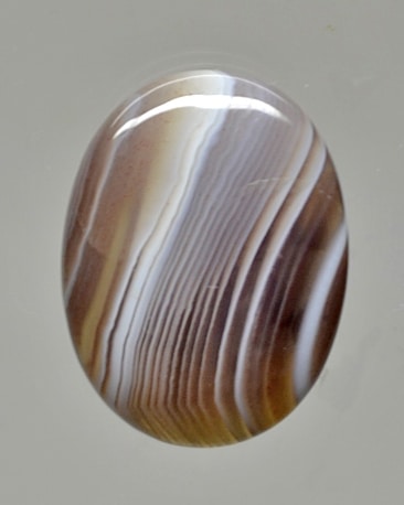 A brown and white agate cabochon on a white background.