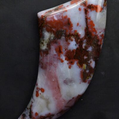 A piece of red and white jasper on a black surface.