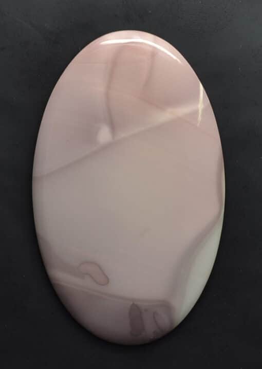 A round piece of pink agate on a black surface.
