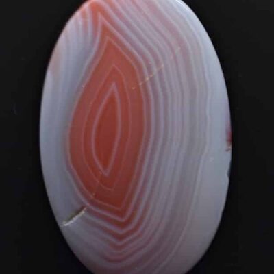 An orange and white agate stone on a black surface.