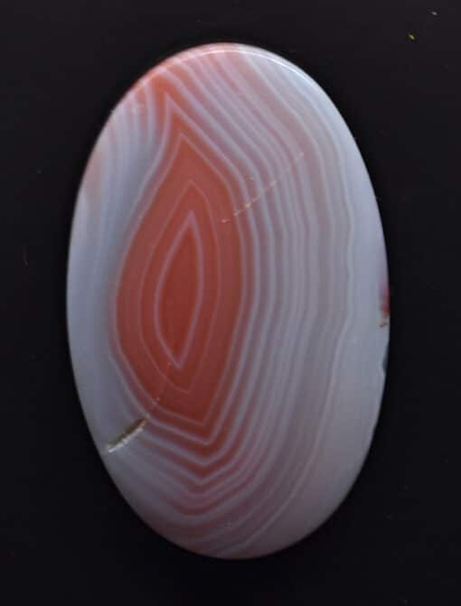 An orange and white agate stone on a black surface.