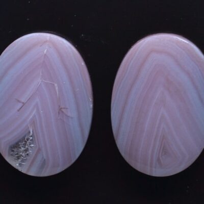 Two pink agate oval cabochons on a black surface.