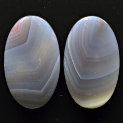 Two oval agate cabochons on a black surface.