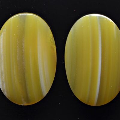 Two yellow agate oval cabochons on a black surface.