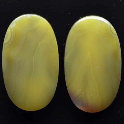 Two yellow agate oval cabochons on a black surface.