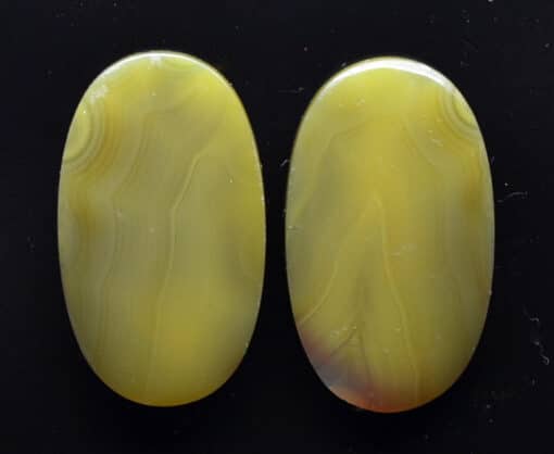 Two yellow agate oval cabochons on a black surface.