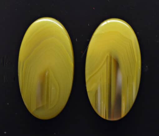 Two yellow agate oval cabochons on a black surface.