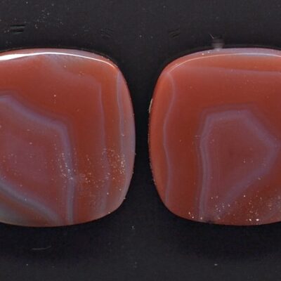 A pair of red agate cabochons on a black surface.