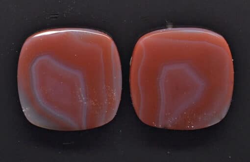 A pair of red agate cabochons on a black surface.