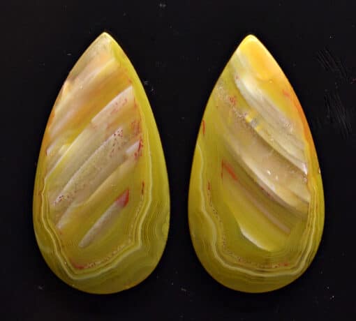 Two yellow agate teardrops on a black surface.