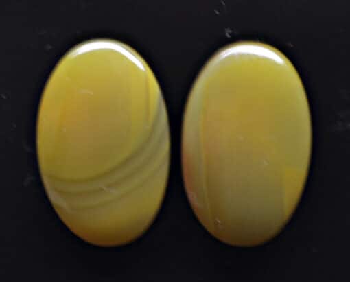 Two yellow agate oval cabochons on a black background.