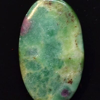 A green and purple stone cabochon on a black surface.