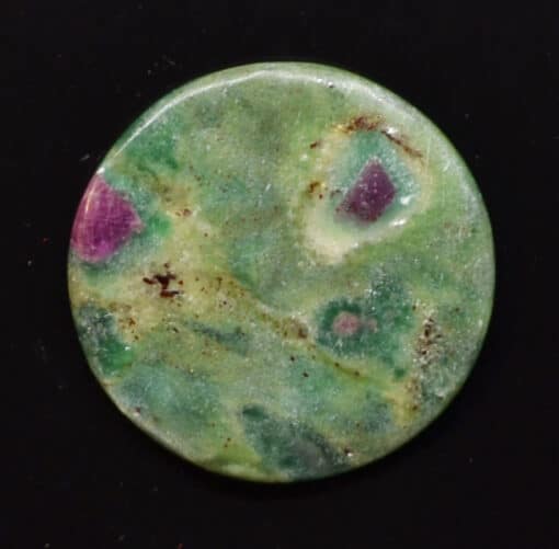 A green and purple colored stone on a black surface.