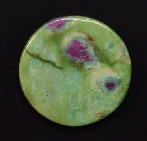 A green and purple button on a black surface.