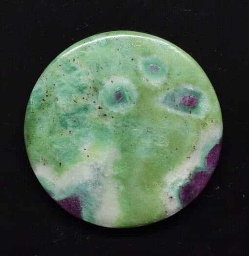 A green and purple agate button on a black surface.