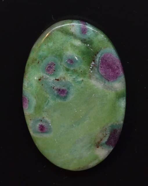 A green and purple stone cabochon on a black surface.