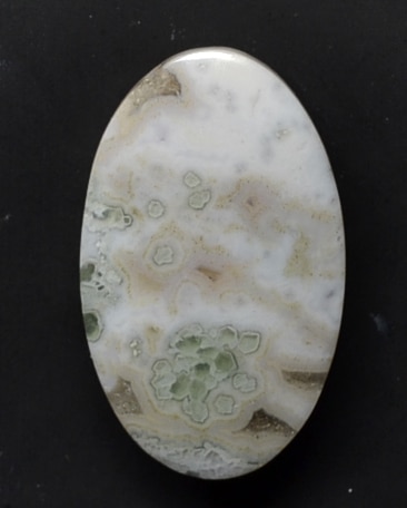A white and green agate cabochon on a black background.