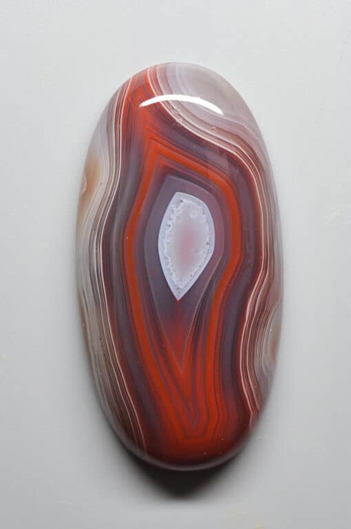 An orange and white agate pendant on a white surface.