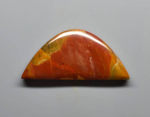 A piece of red and orange jasper on a gray surface.